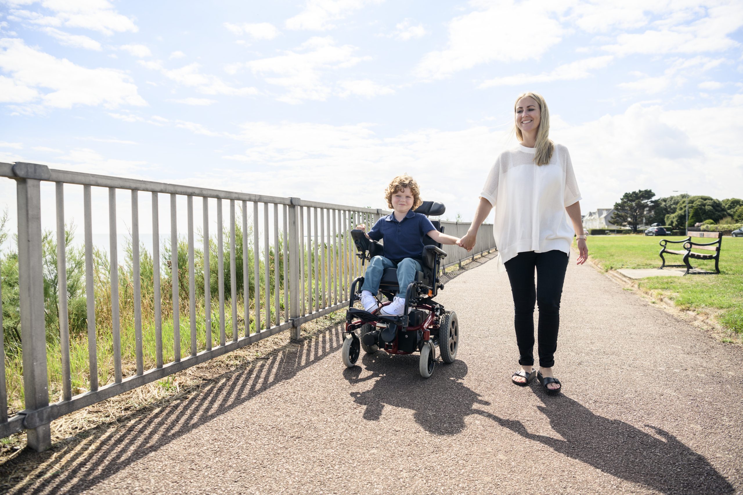 Disabled boy in wheelchair holding mother's hand on path